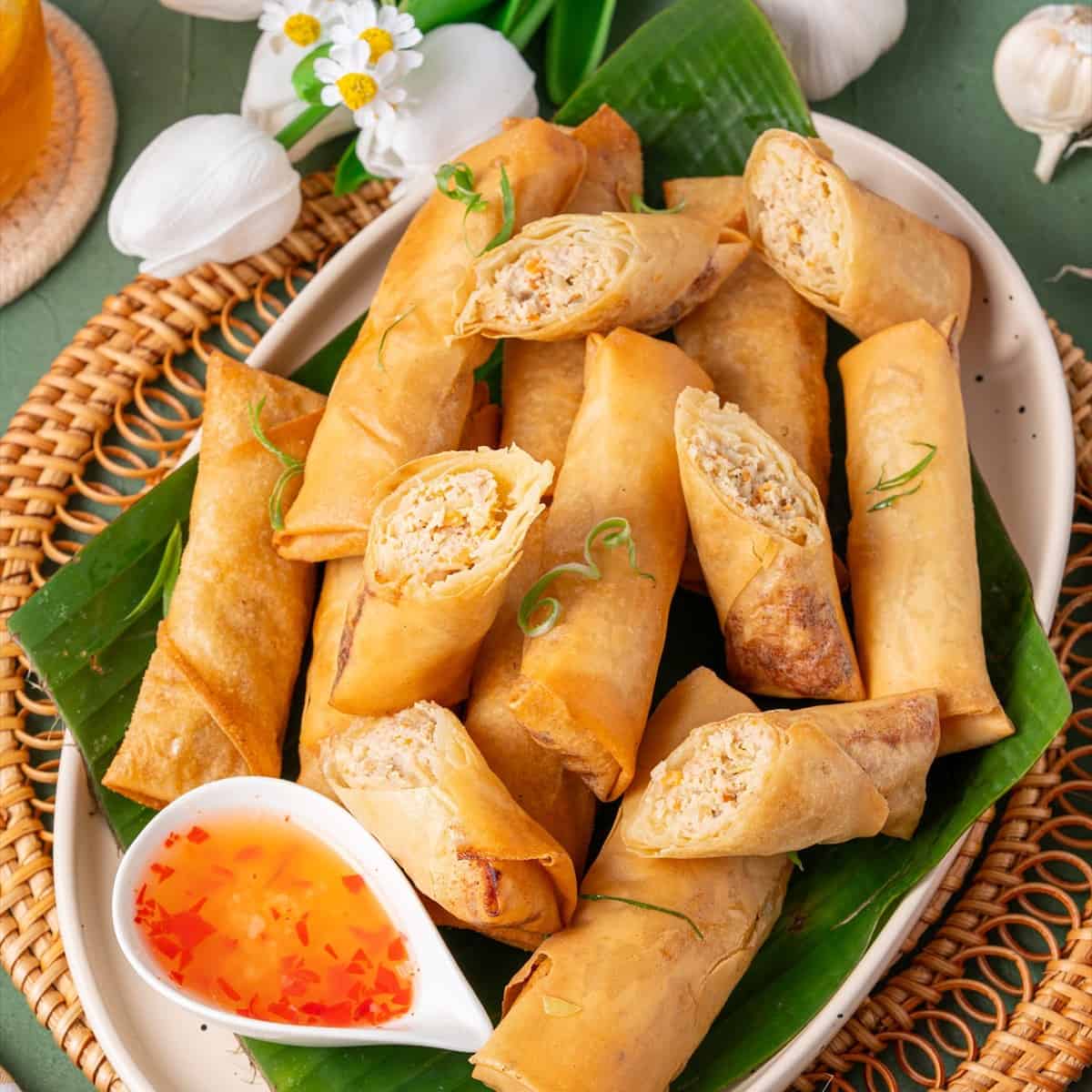 Golden fried Filipino lumpia on a banana leaf lined plate with sweet chili dipping sauce