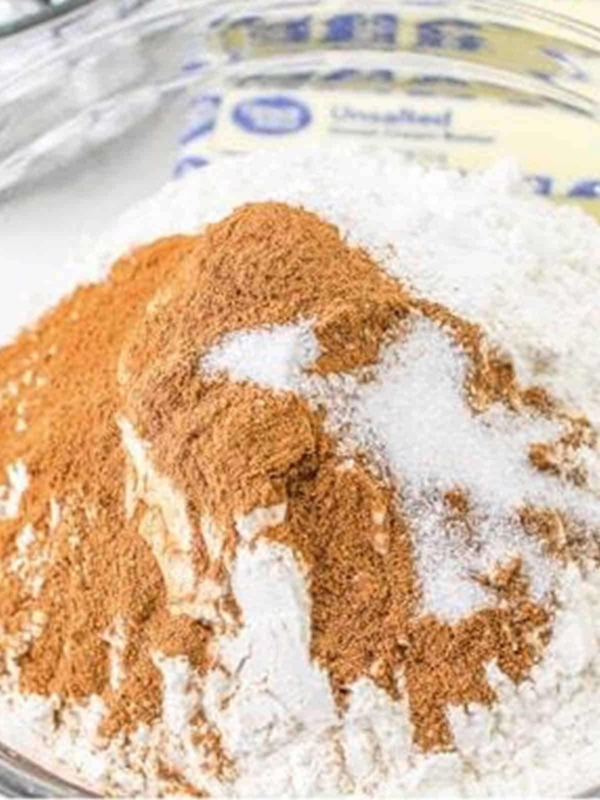 Flour, baking powder, baking soda, salt, cinnamon, and pumpkin spice whisked together in a bowl for pumpkin cookies.