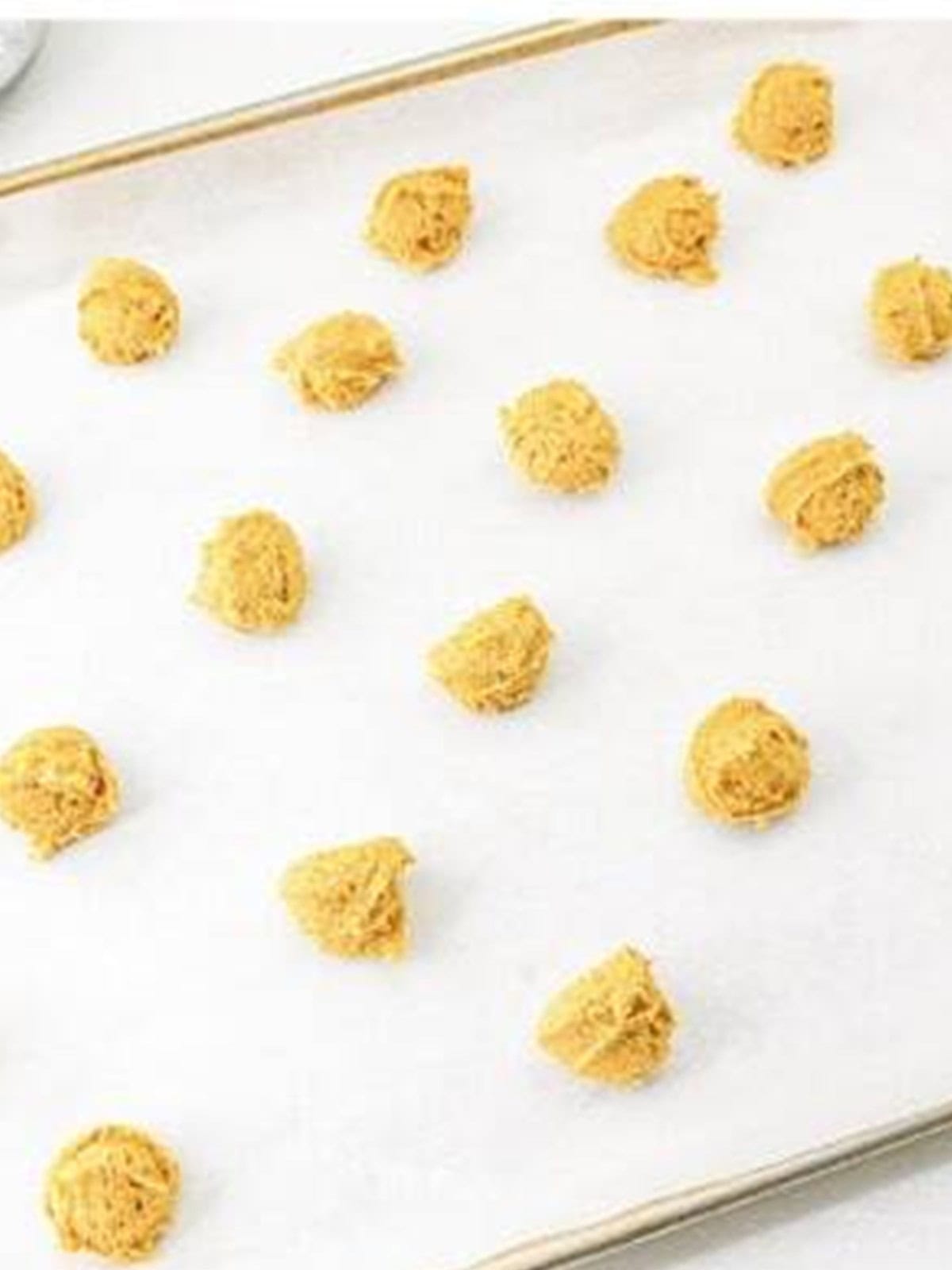 Scooped pumpkin cookie dough balls placed on a parchment lined baking sheet.
