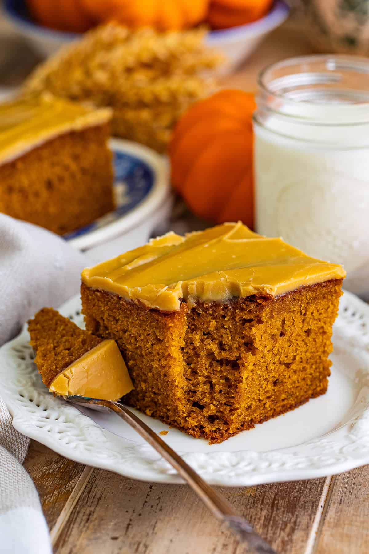 A slice of pumpkin spice cake with a bite removed showing the moist tender crumb under the brown sugar frosting.