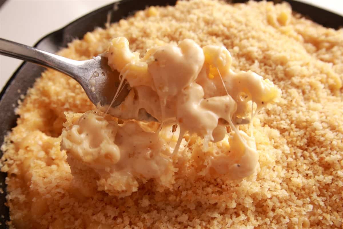 A spoonful of creamy smoked mac and cheese lifted from the cast iron skillet with a gooey cheese pull.