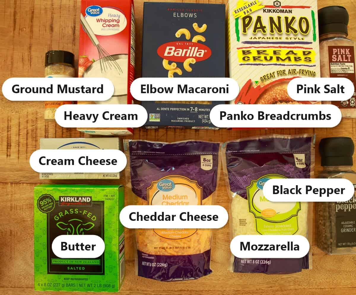 Labeled ingredients for smoked mac and cheese including elbow macaroni, heavy cream, cream cheese, cheddar cheese, mozzarella, butter, panko breadcrumbs, ground mustard, pink salt, and black pepper.