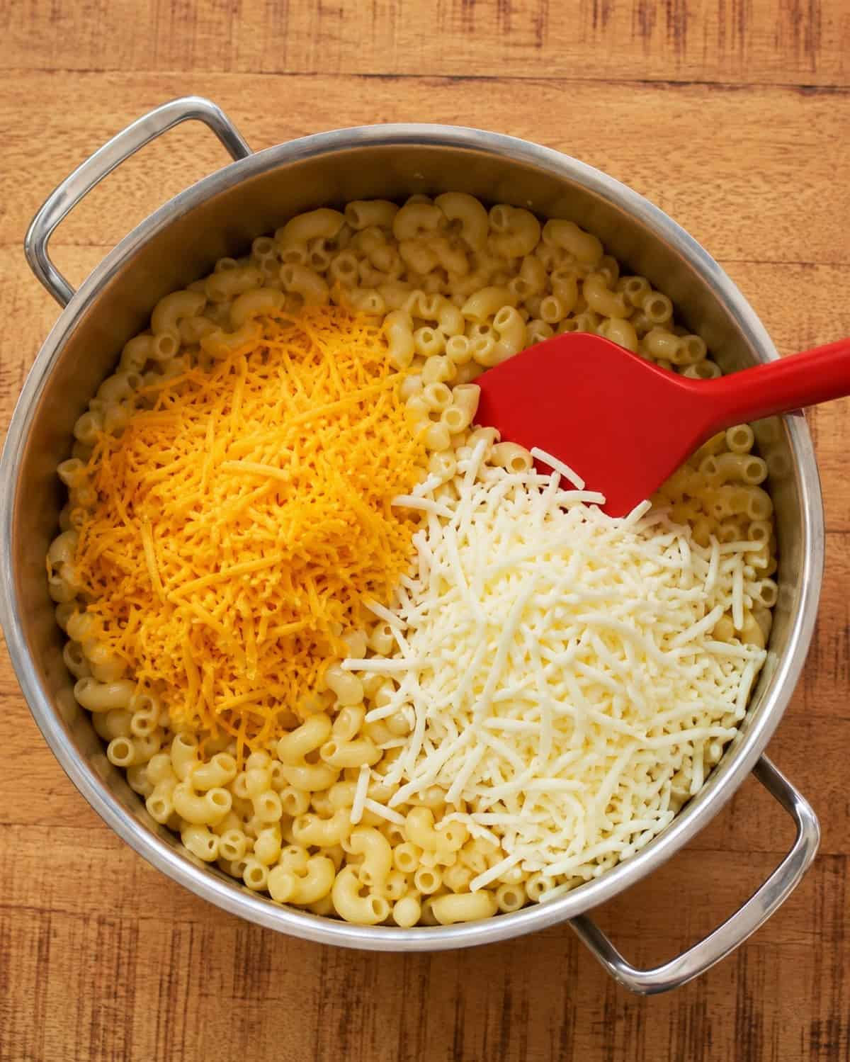 Cooked elbow macaroni topped with shredded cheddar and mozzarella cheese in a large pot.