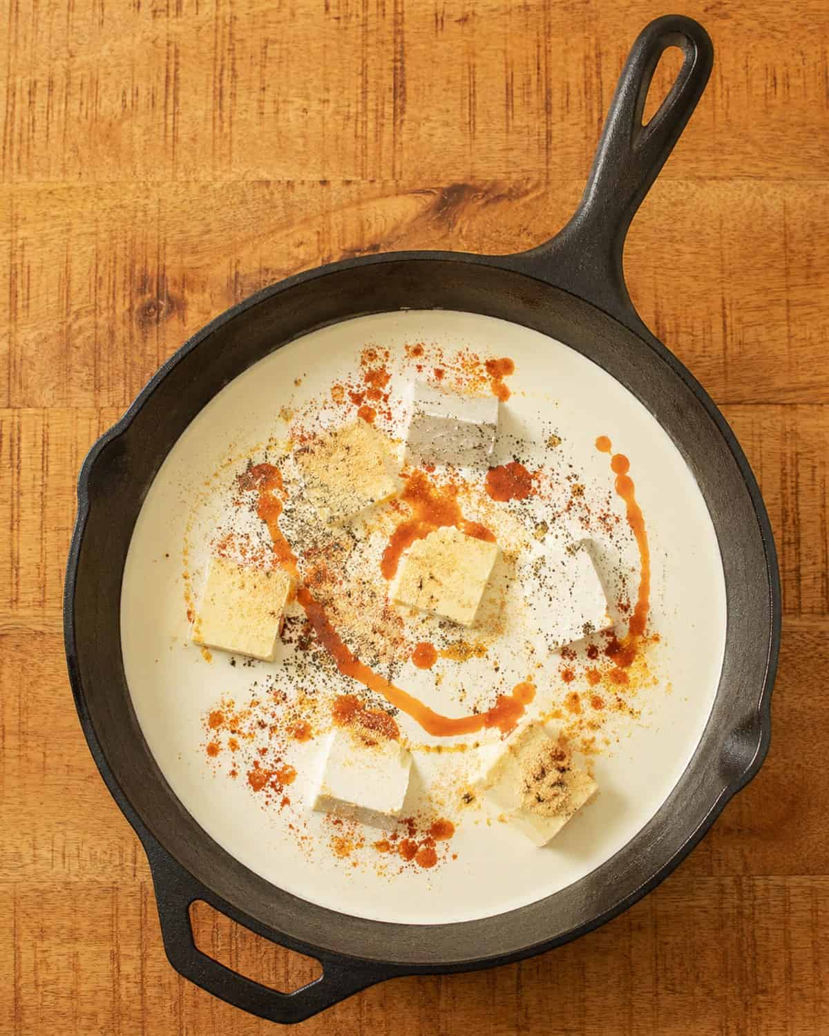 Heavy cream, butter, cream cheese, and seasonings combined in a cast iron skillet for smoked mac and cheese sauce.