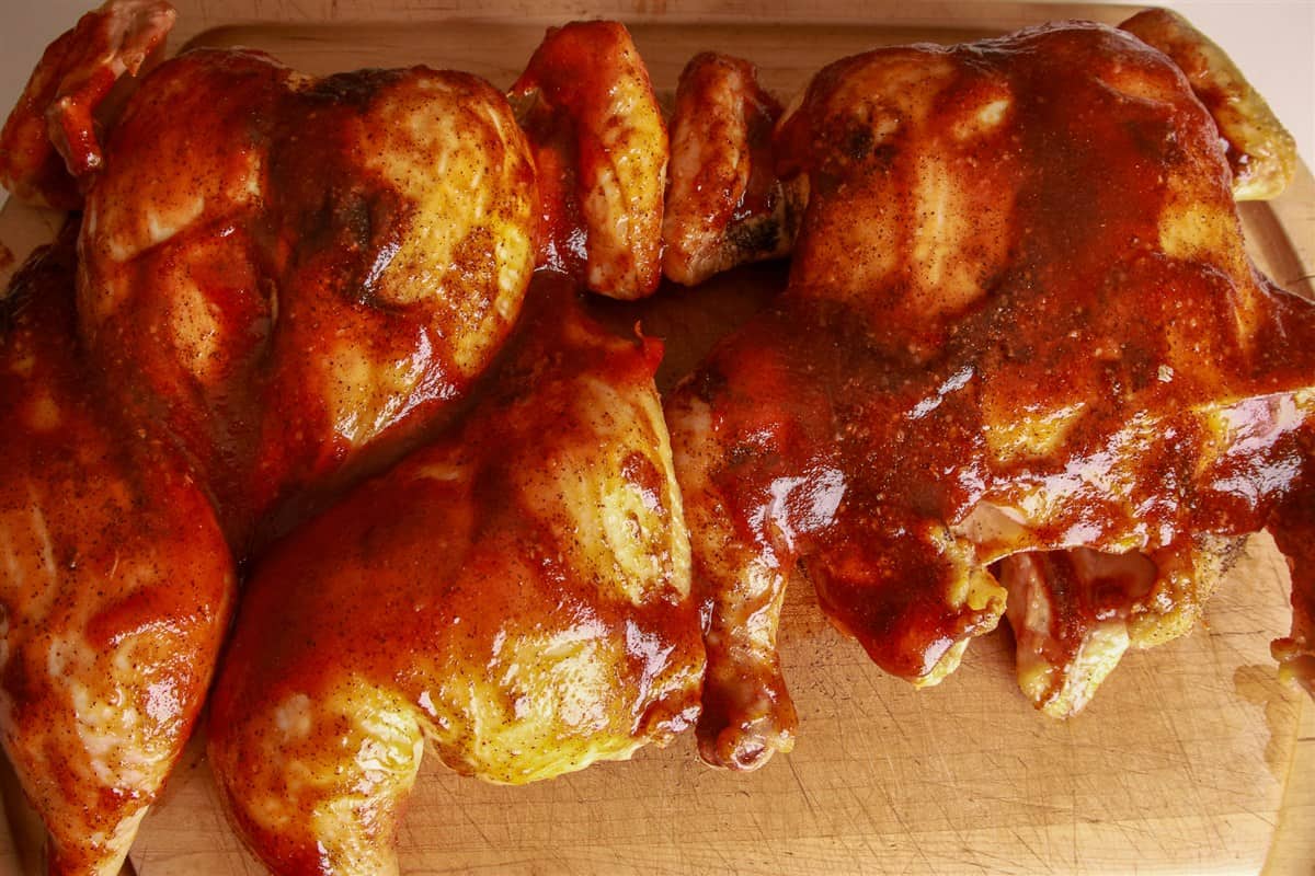 Carved smoked spatchcock chicken pieces glazed with barbecue sauce on a wooden cutting board.