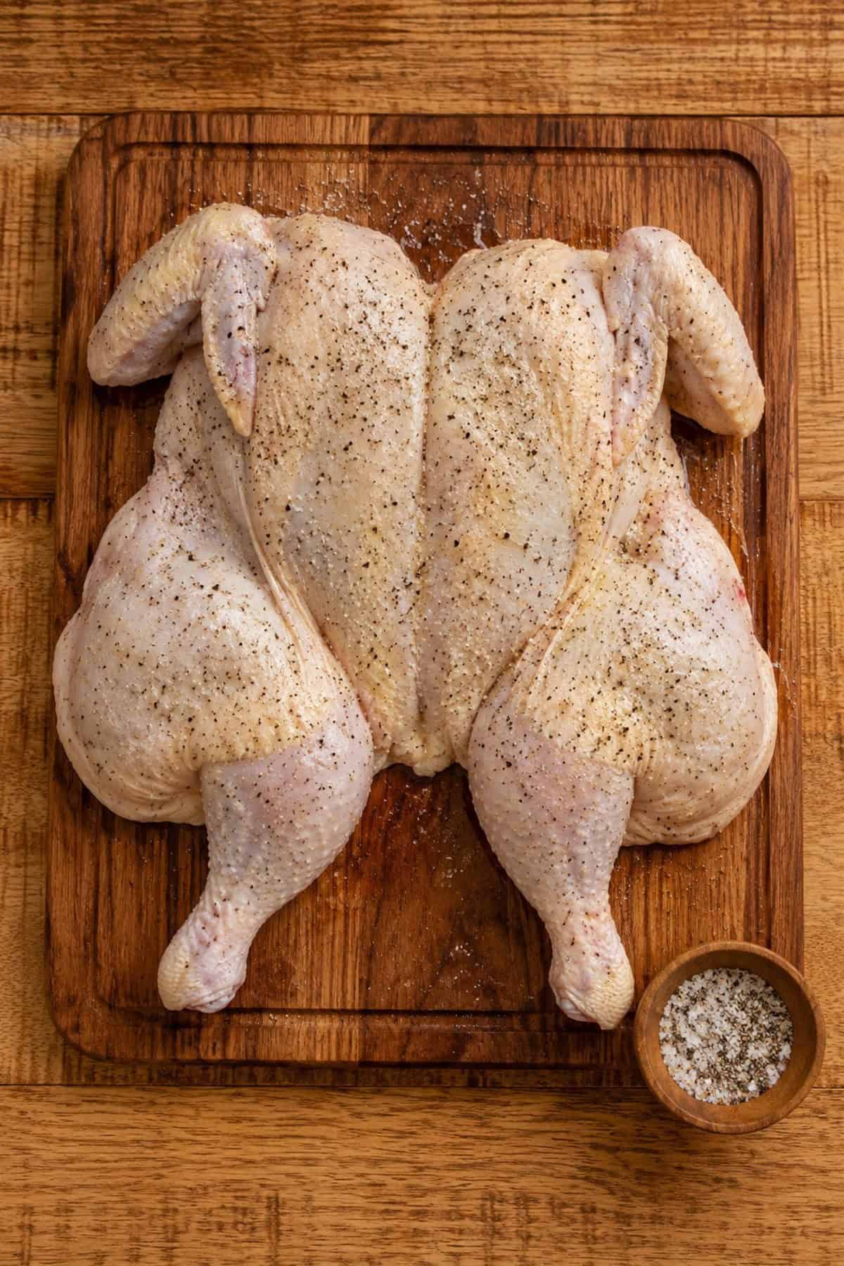 A flattened raw spatchcock chicken rubbed with oil and seasoned with kosher salt and black pepper.