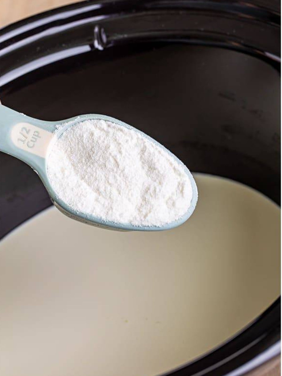 Whisking white chocolate powder into heavy cream in a slow cooker to start Witches Brew hot chocolate.