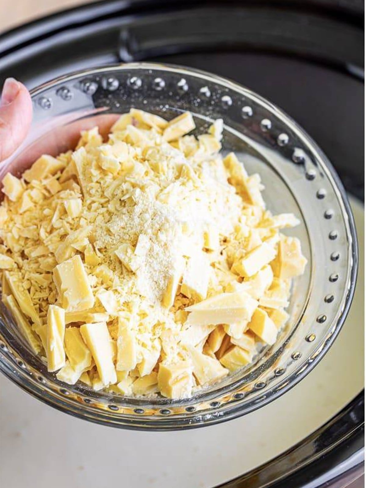Adding chopped white chocolate, whole milk, and sweetened condensed milk to the slow cooker for Witches Brew.