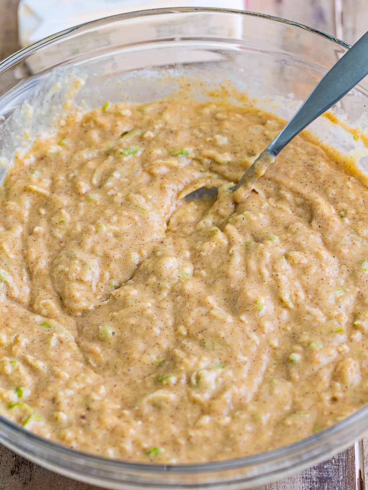 Apple spice cake batter with grated Granny Smith apple stirred through in a glass bowl.