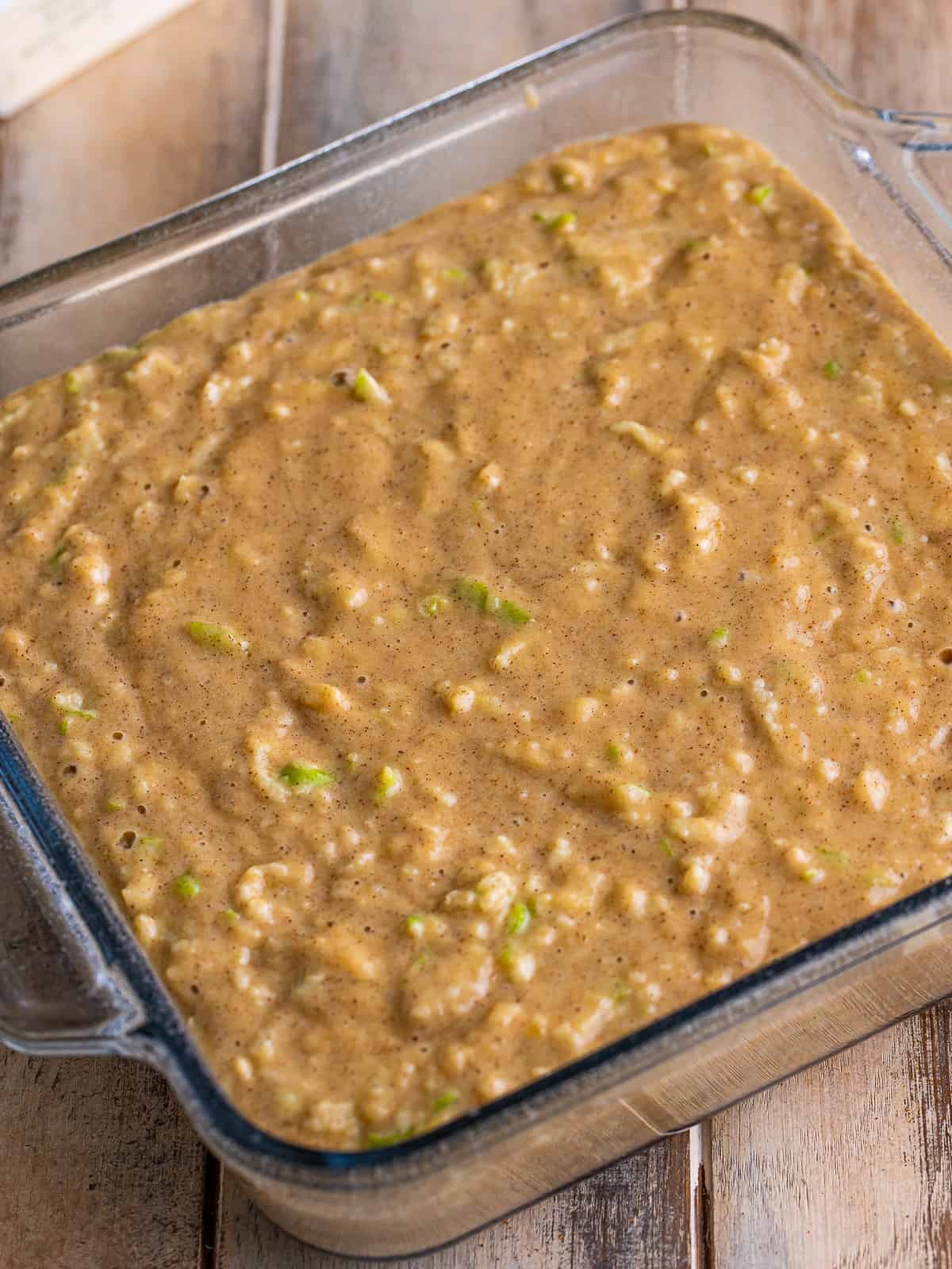 Apple spice cake batter spread level in a greased 8x8 glass baking dish.