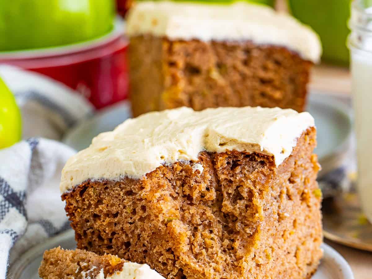 A fork lifting a bite from a frosted apple spice cake slice showing the tender crumb.