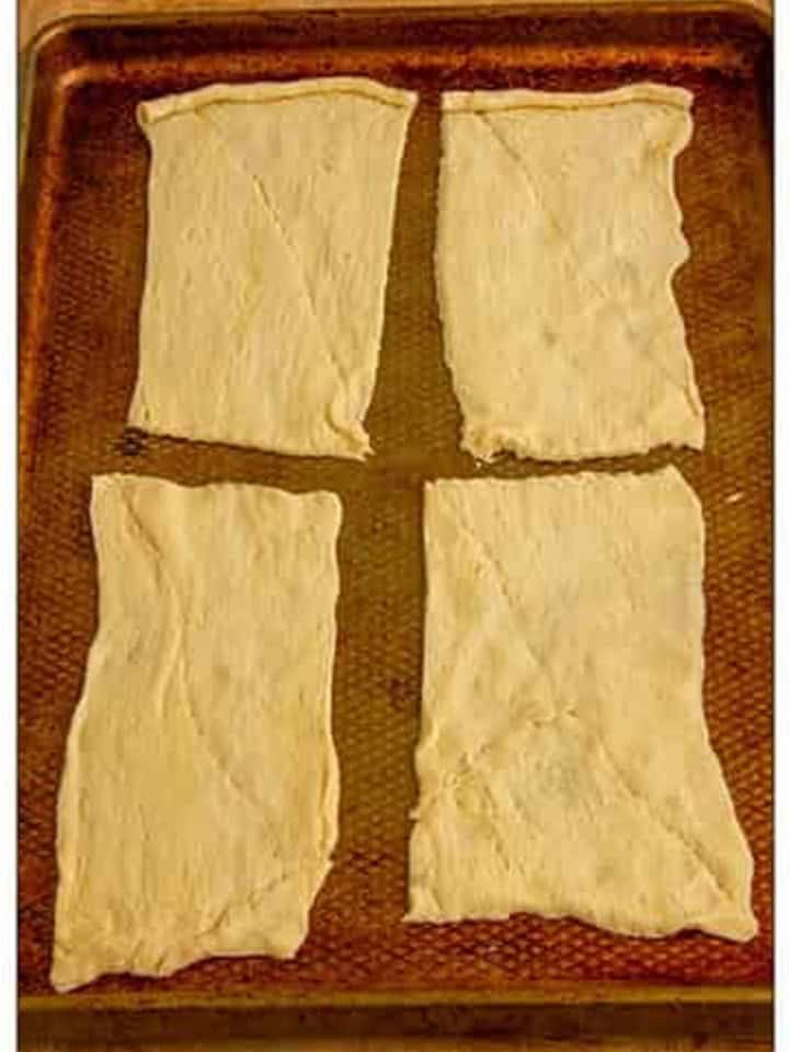 Crescent roll dough separated into four rectangles on a baking sheet.