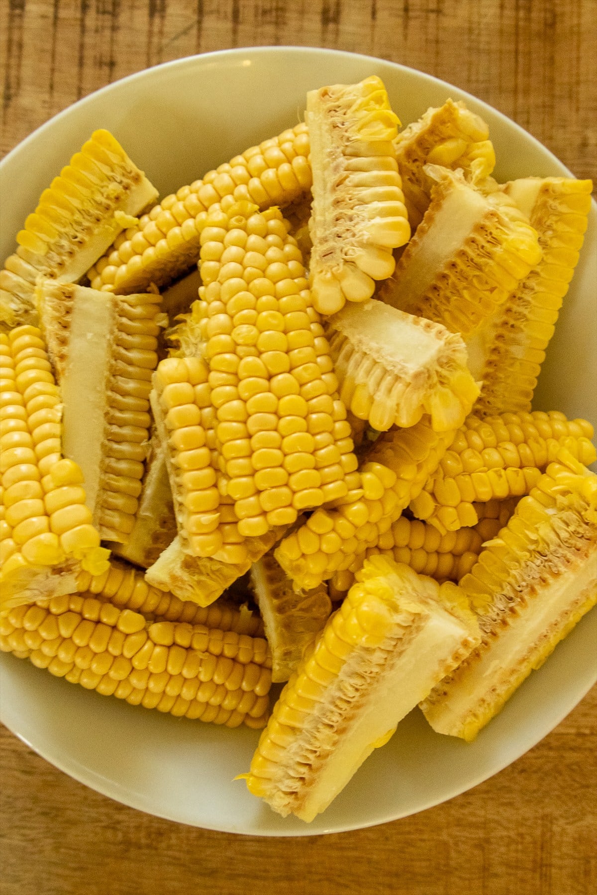 Raw corn ribs cut into long quarters piled in a white bowl.
