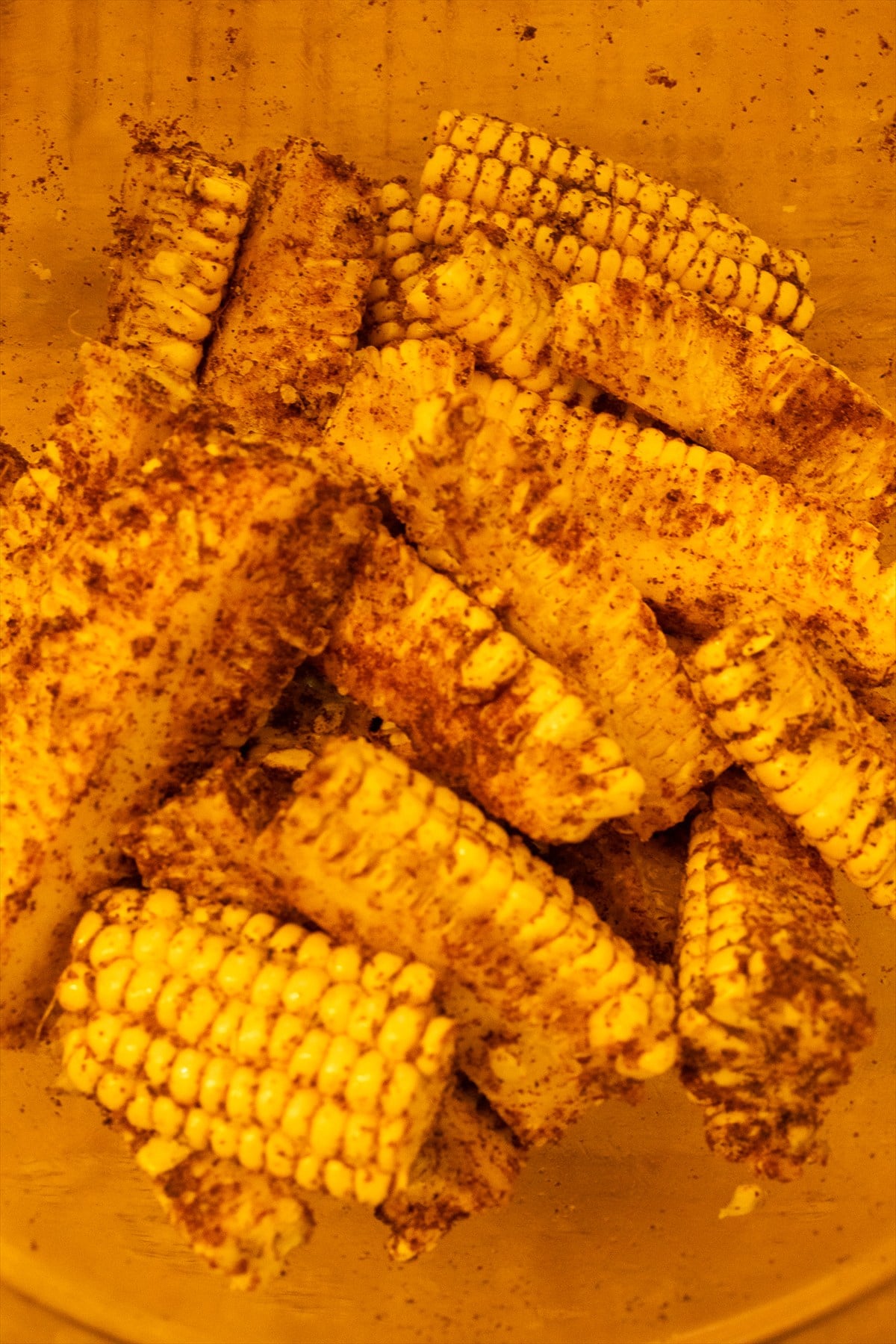 Corn ribs tossed with olive oil and a smoky seasoning blend in a mixing bowl.