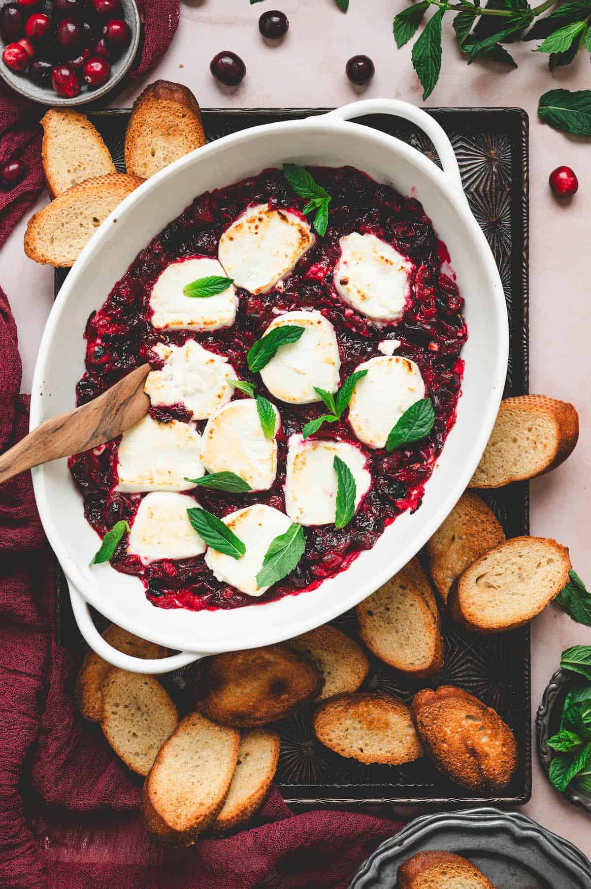 Warm goat cheese rounds baked in a white dish of cranberry sauce with fresh basil, served with toasted baguette slices.