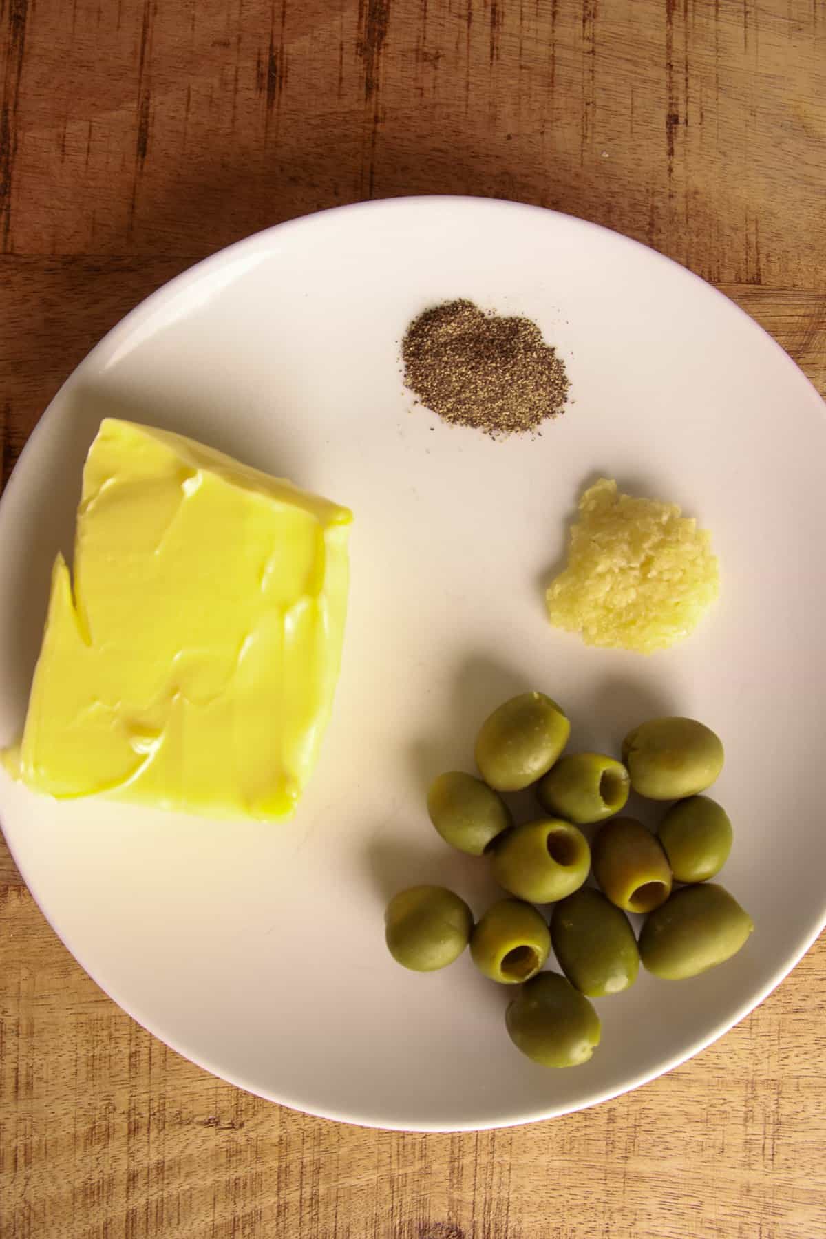 Softened butter with pitted green olives, garlic, and black pepper for garlic green olive compound butter.