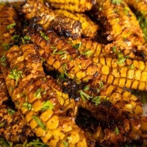 Grilled corn ribs stacked on a white platter with charred edges, garlic butter, and chopped parsley.