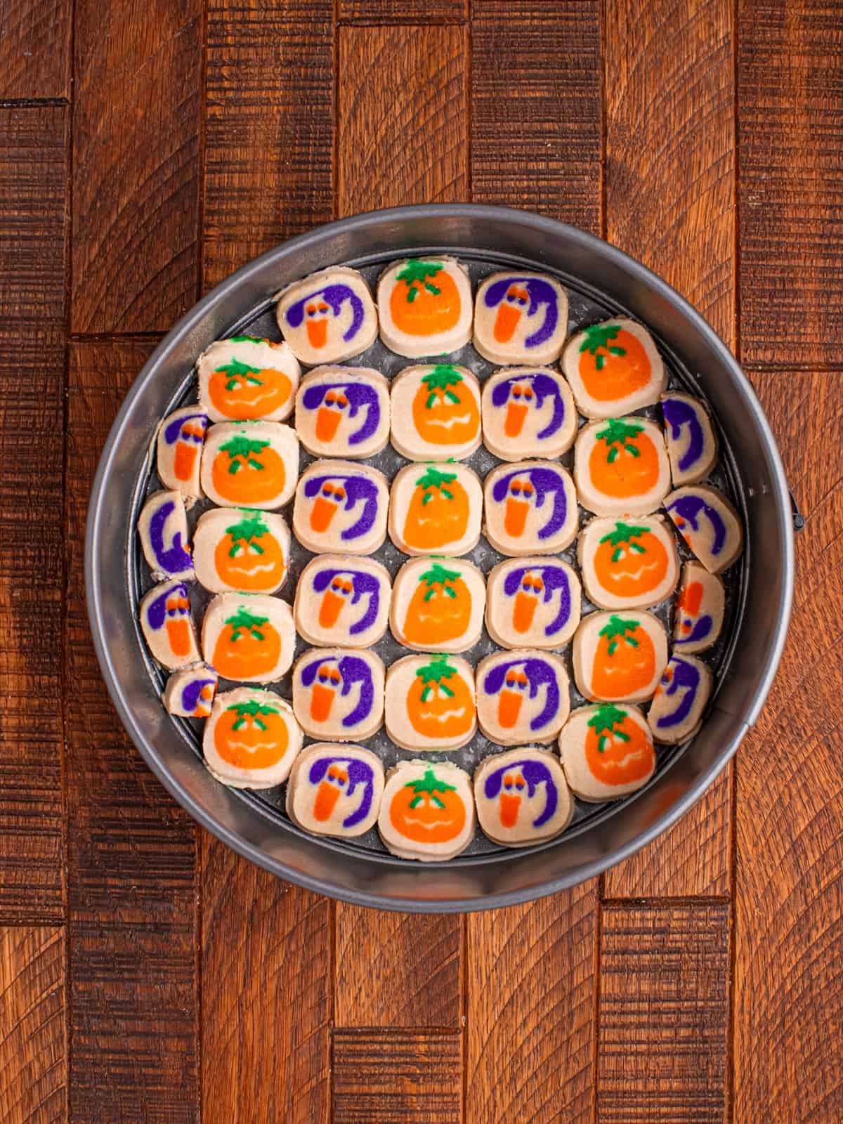 Pumpkin and ghost sugar cookie dough rounds arranged in rows in a springform pan.