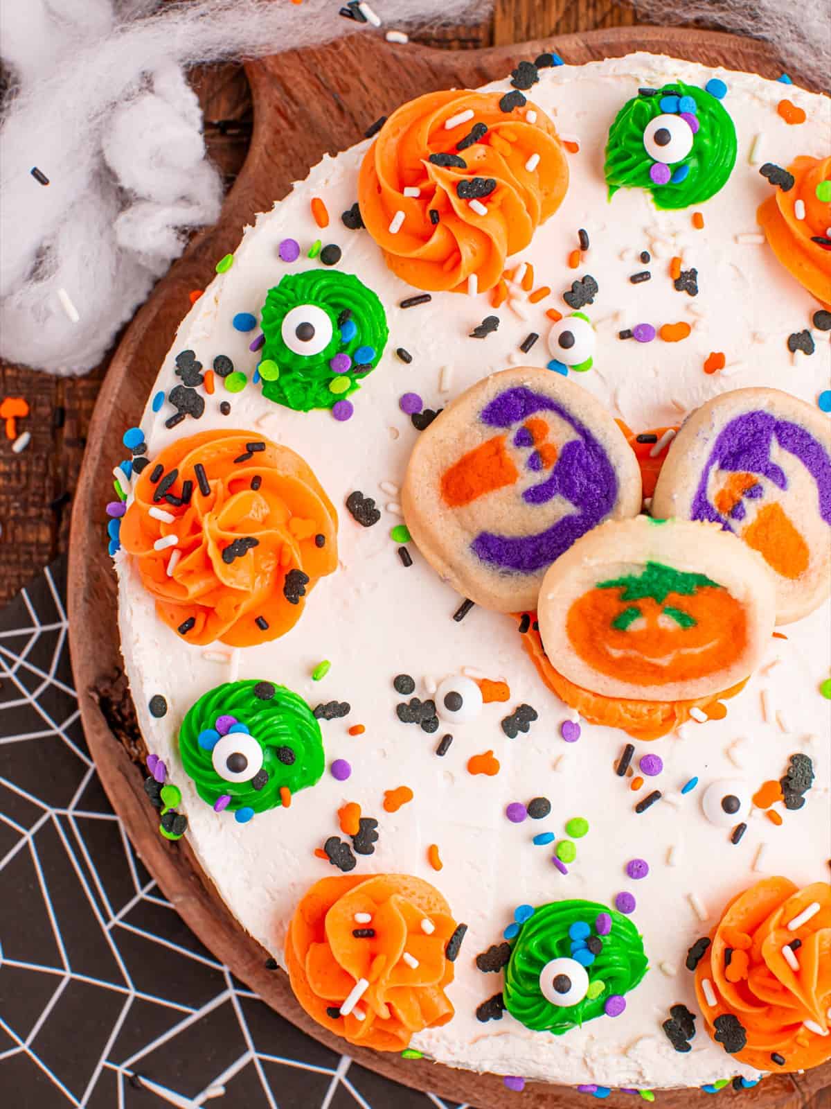 Close up of the decorated Halloween sugar cookie cheesecake with frosting swirls, candy eyes, sprinkles, and a pumpkin cookie on top.