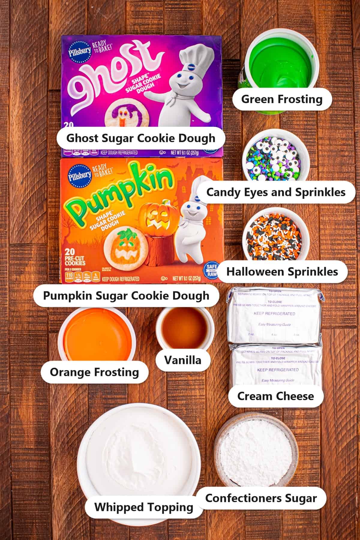 Labeled ingredients for Halloween sugar cookie cheesecake including ghost and pumpkin sugar cookie dough, cream cheese, confectioners sugar, vanilla, whipped topping, orange and green frosting, candy eyes, and Halloween sprinkles.