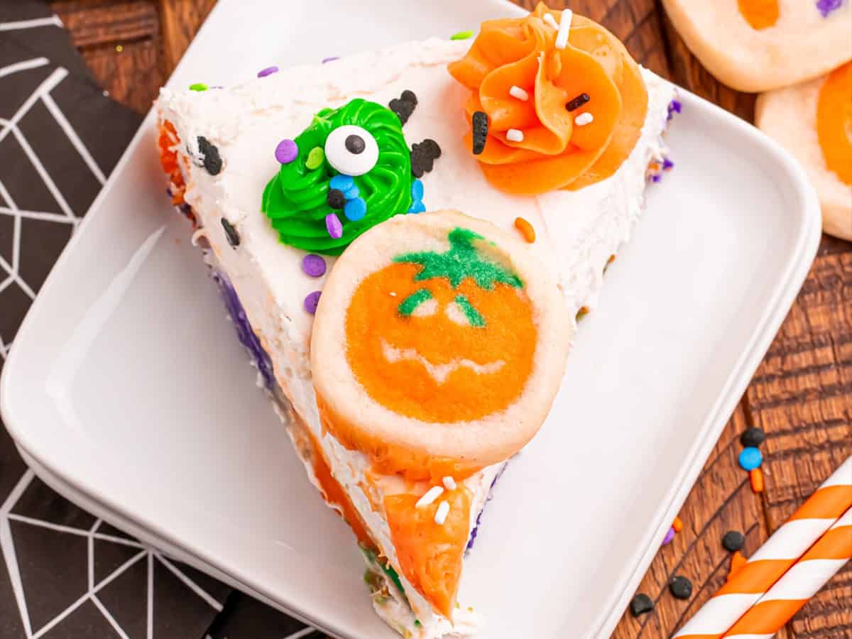 A slice of Halloween sugar cookie cheesecake on a white plate showing the cookie crust and creamy filling.