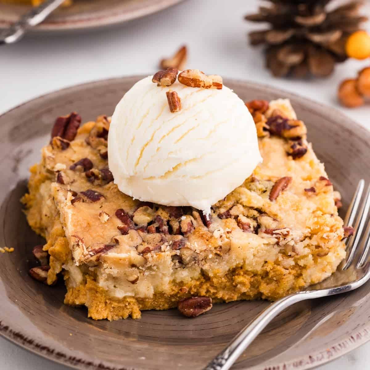 A square of pumpkin crunch cake topped with pecans and a scoop of vanilla ice cream.