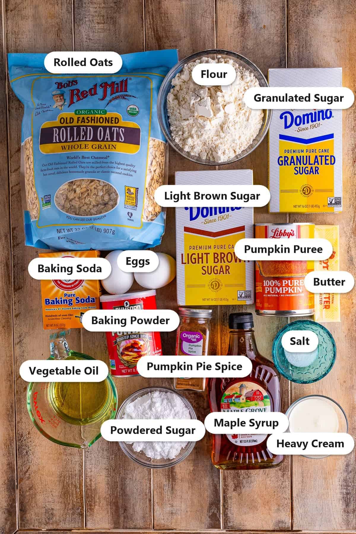 Labeled ingredients for pumpkin oatmeal muffins including rolled oats, flour, granulated sugar, light brown sugar, pumpkin puree, butter, baking soda, baking powder, eggs, pumpkin pie spice, salt, vegetable oil, maple syrup, powdered sugar and heavy cream.
