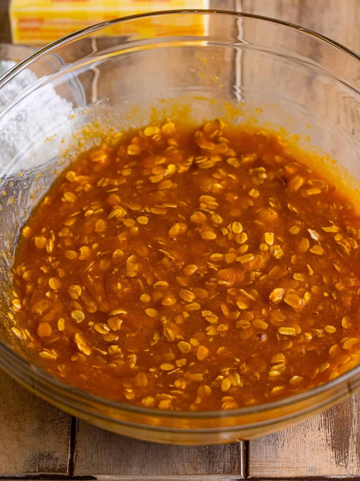 Rolled oats stirred into pumpkin puree, oil, sugars, maple syrup and eggs in a glass bowl.