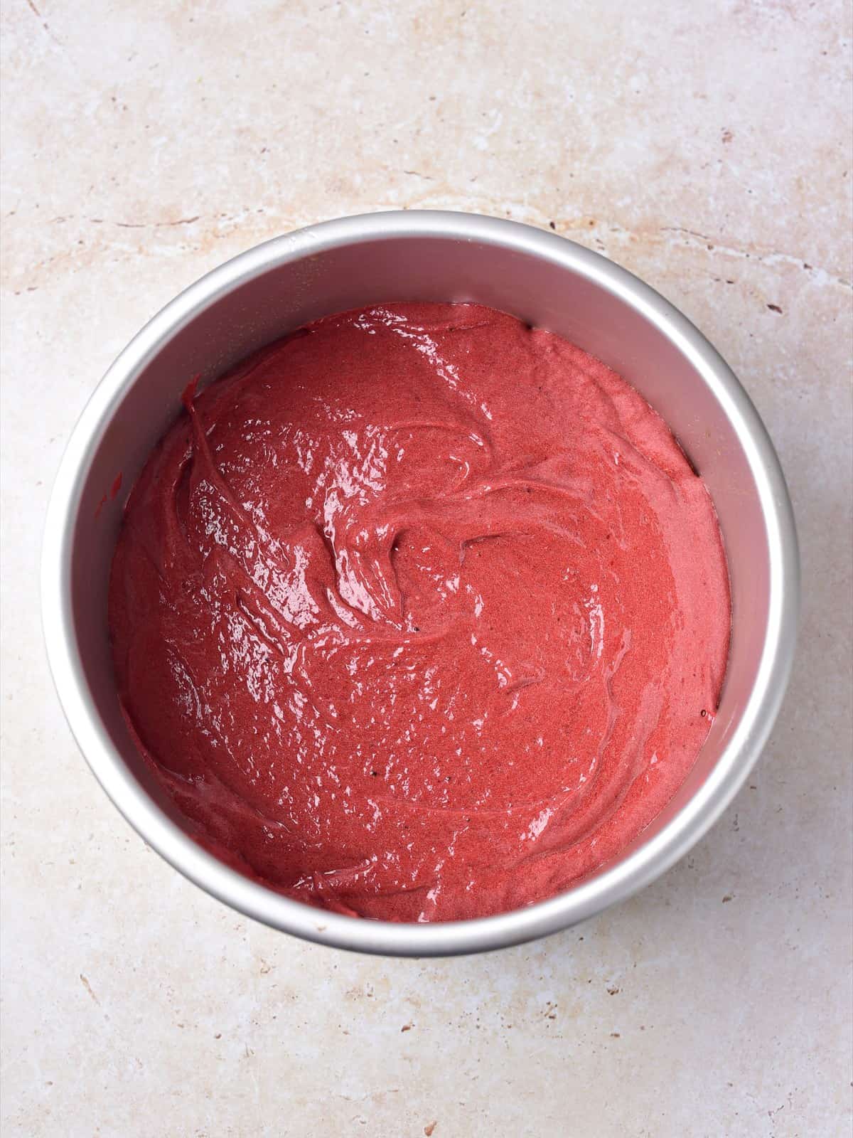 Smooth red velvet cake batter spread in a round 7 inch cake pan.