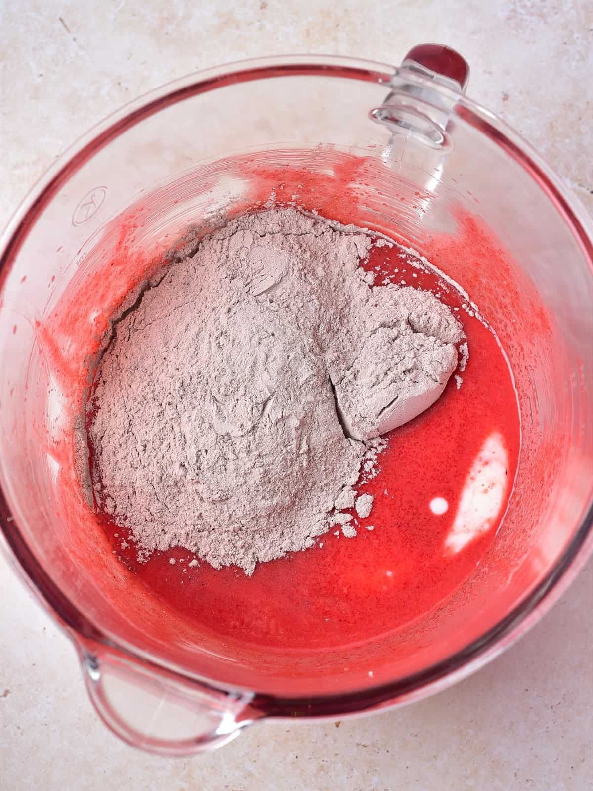 Sifted flour, cocoa powder, baking soda, baking powder, and salt on top of the red batter in a glass bowl.