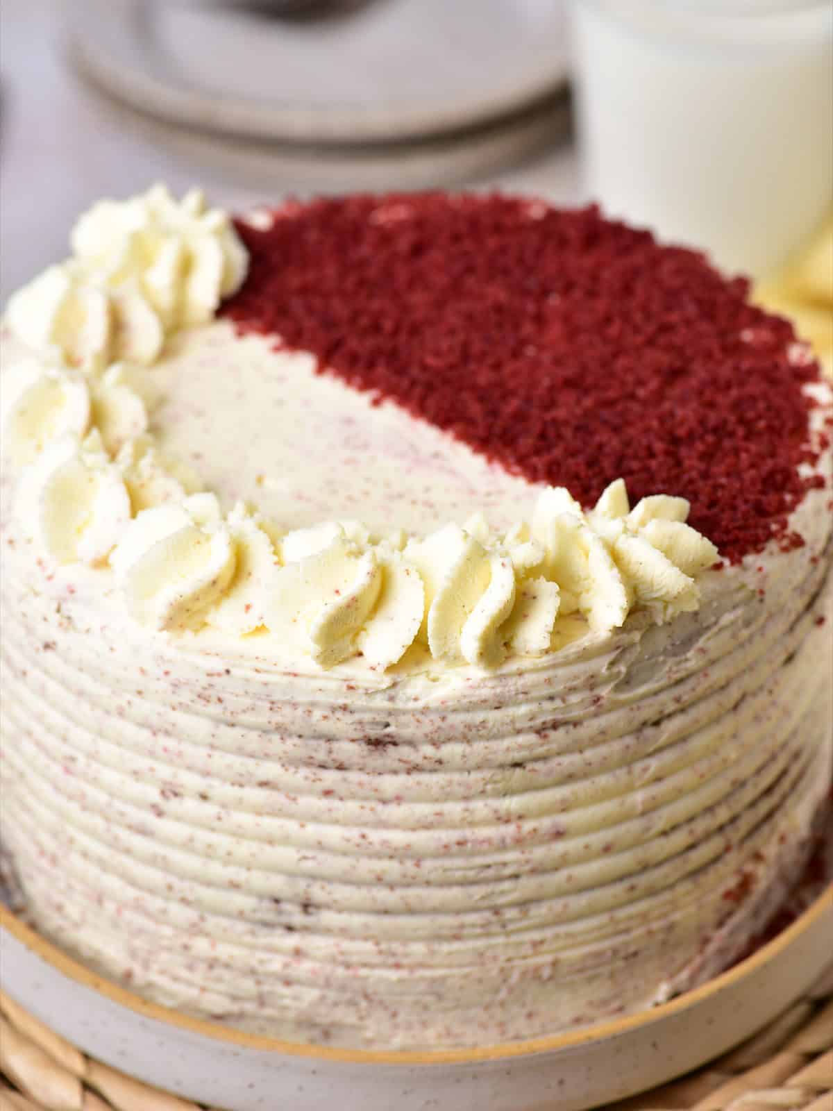 Whole red velvet cake frosted with mascarpone cream, piped rosettes, and red cake crumbs on top.
