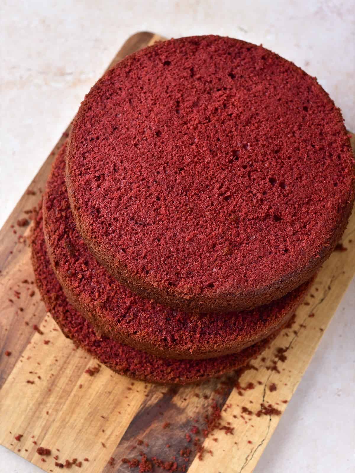 Three trimmed red velvet cake layers stacked on a wooden board.