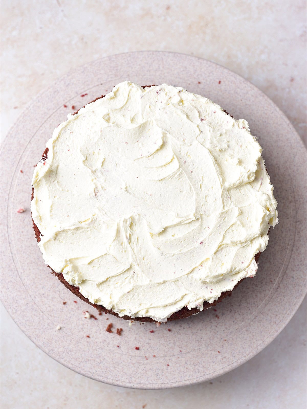 Mascarpone frosting spread over a red velvet cake layer with a spatula.