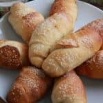 A plate of buttery salt bread rolls topped with flaky salt, golden on top with crisp bottoms.