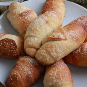 A plate of buttery salt bread rolls topped with flaky salt, golden on top with crisp bottoms.