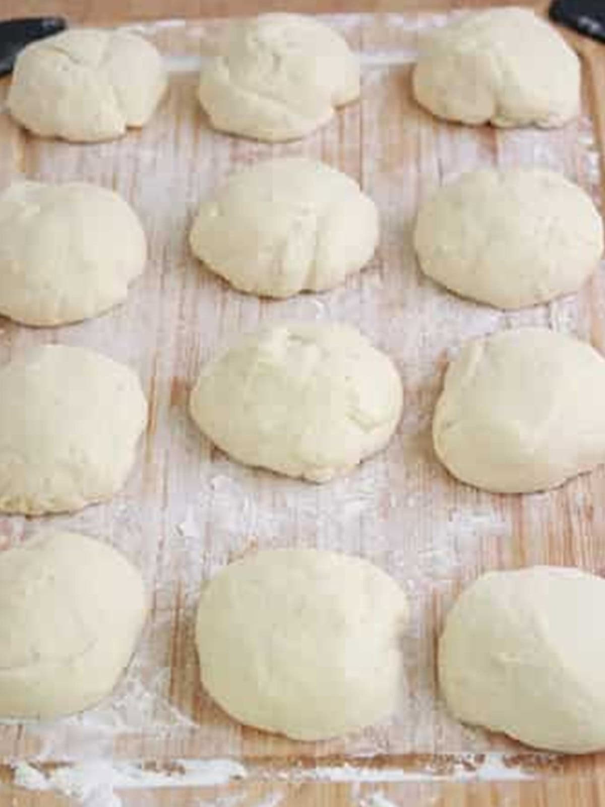 Twelve portioned salt bread dough balls resting on a floured wooden board.
