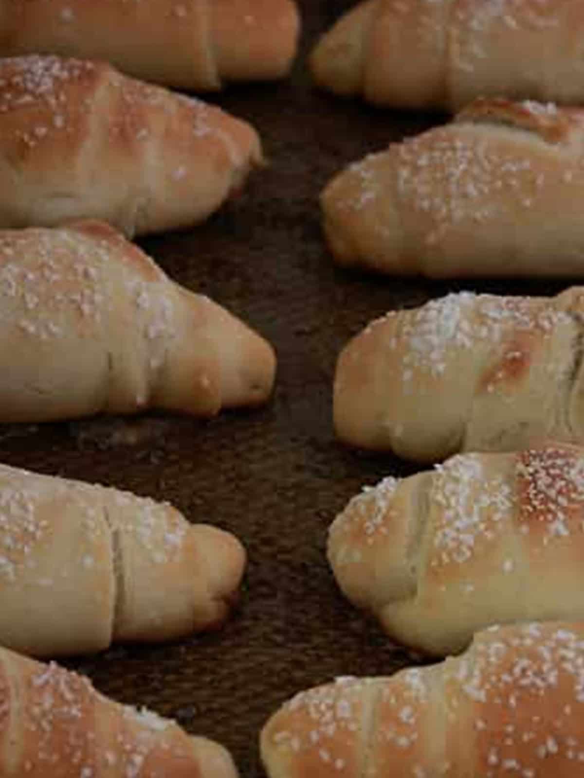 Golden baked salt bread rolls sprinkled with flaky salt on a dark baking pan.