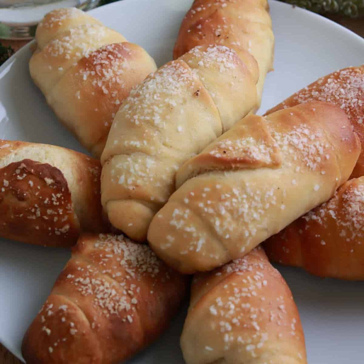A plate of buttery salt bread rolls topped with flaky salt, golden on top with crisp bottoms.
