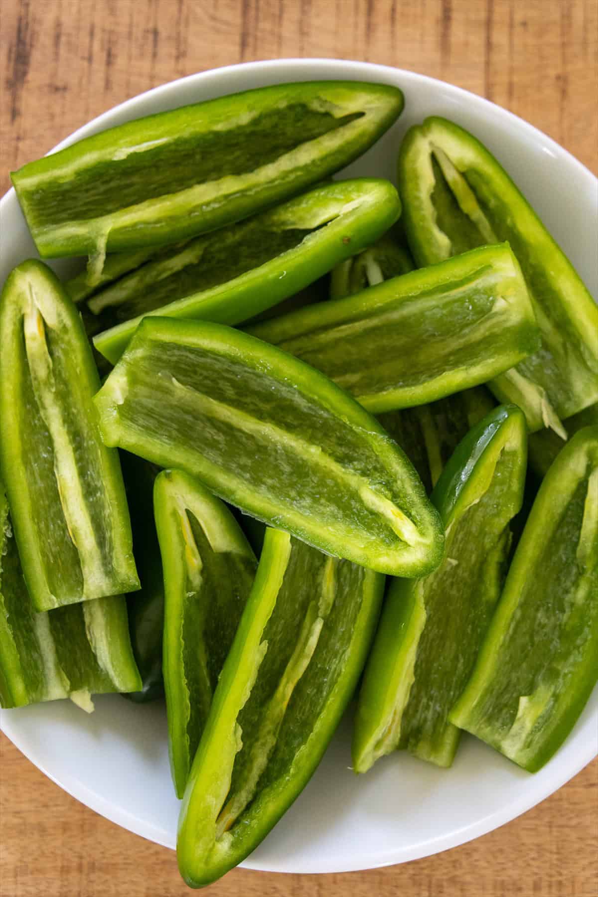 Fresh jalapenos cut in half and seeded in a white bowl.