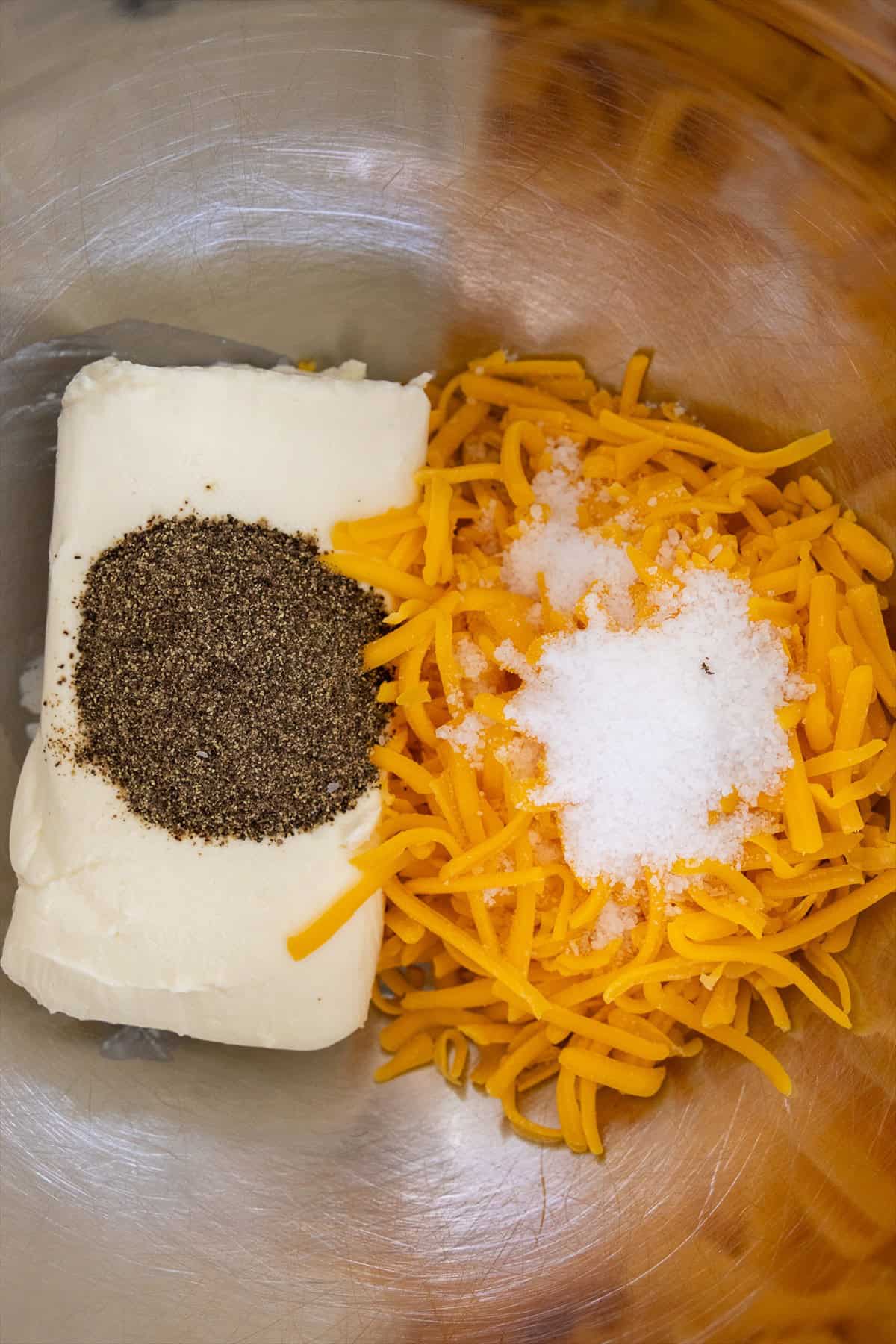 Cream cheese, shredded cheddar, kosher salt, and black pepper in a metal mixing bowl.