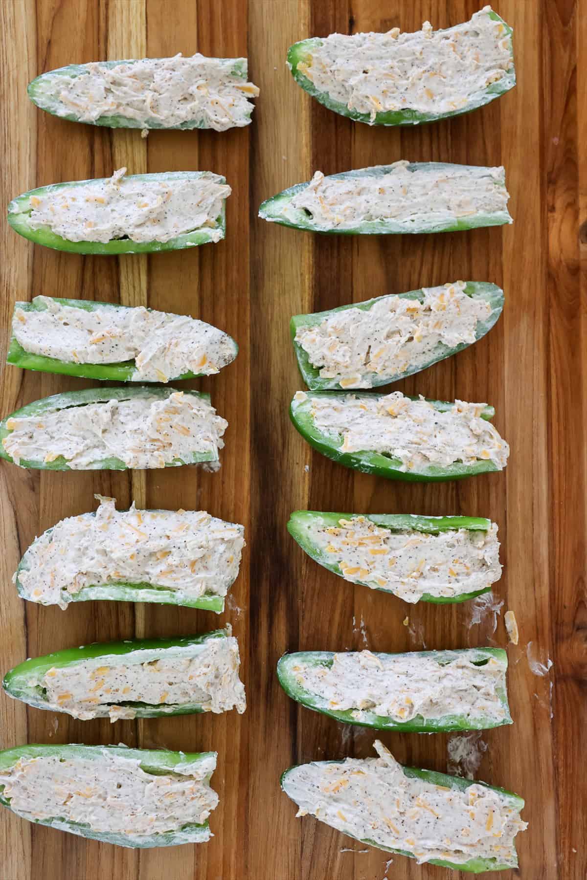 Jalapeno halves filled with cheddar cream cheese filling on a wood cutting board.