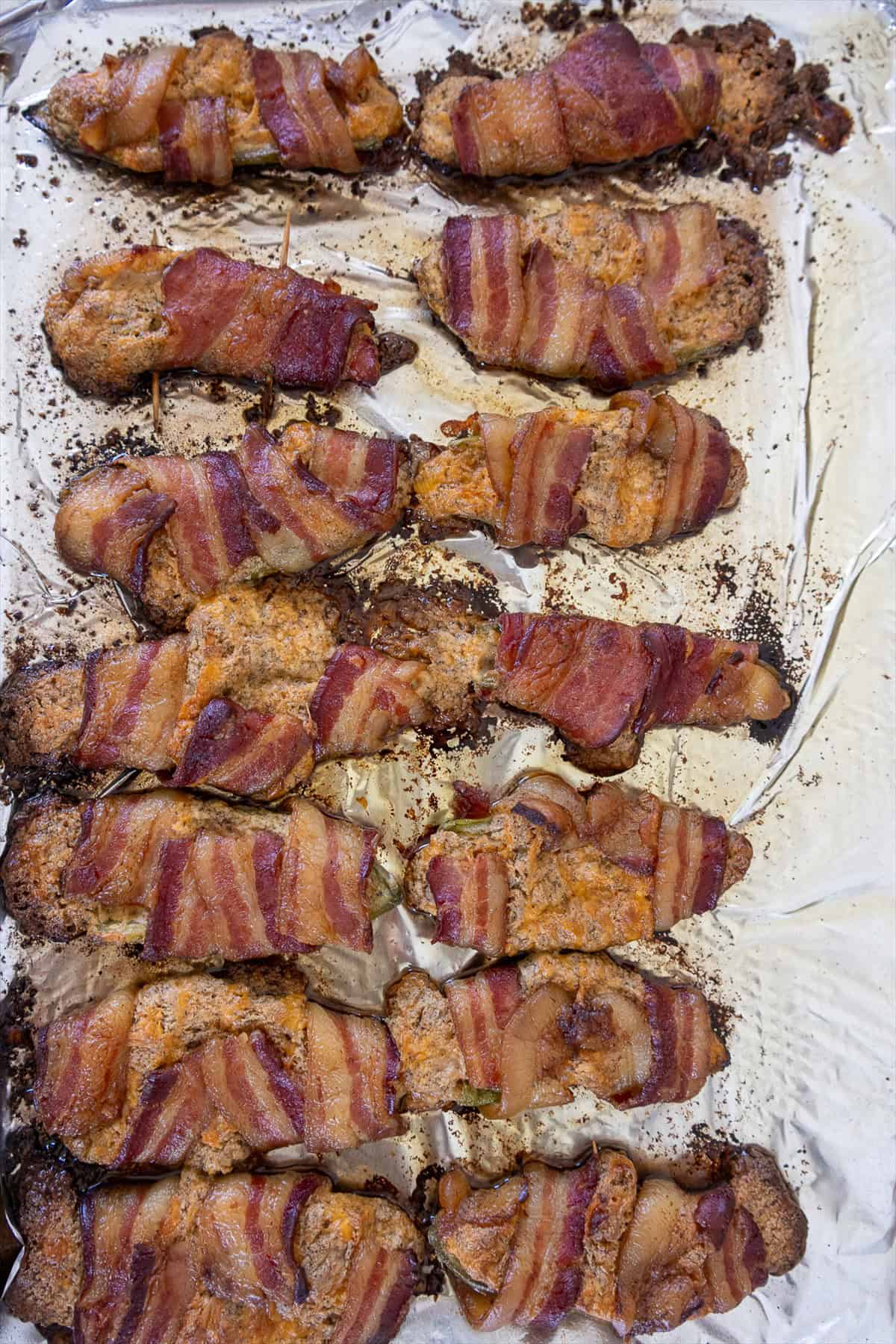 Smoked bacon wrapped jalapeno poppers on a sheet pan with crispy browned bacon.
