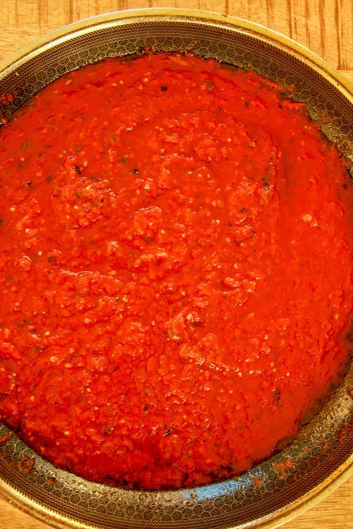 Homemade tomato sauce for smoked pizza simmered in a pan with garlic, basil, and Parmesan.