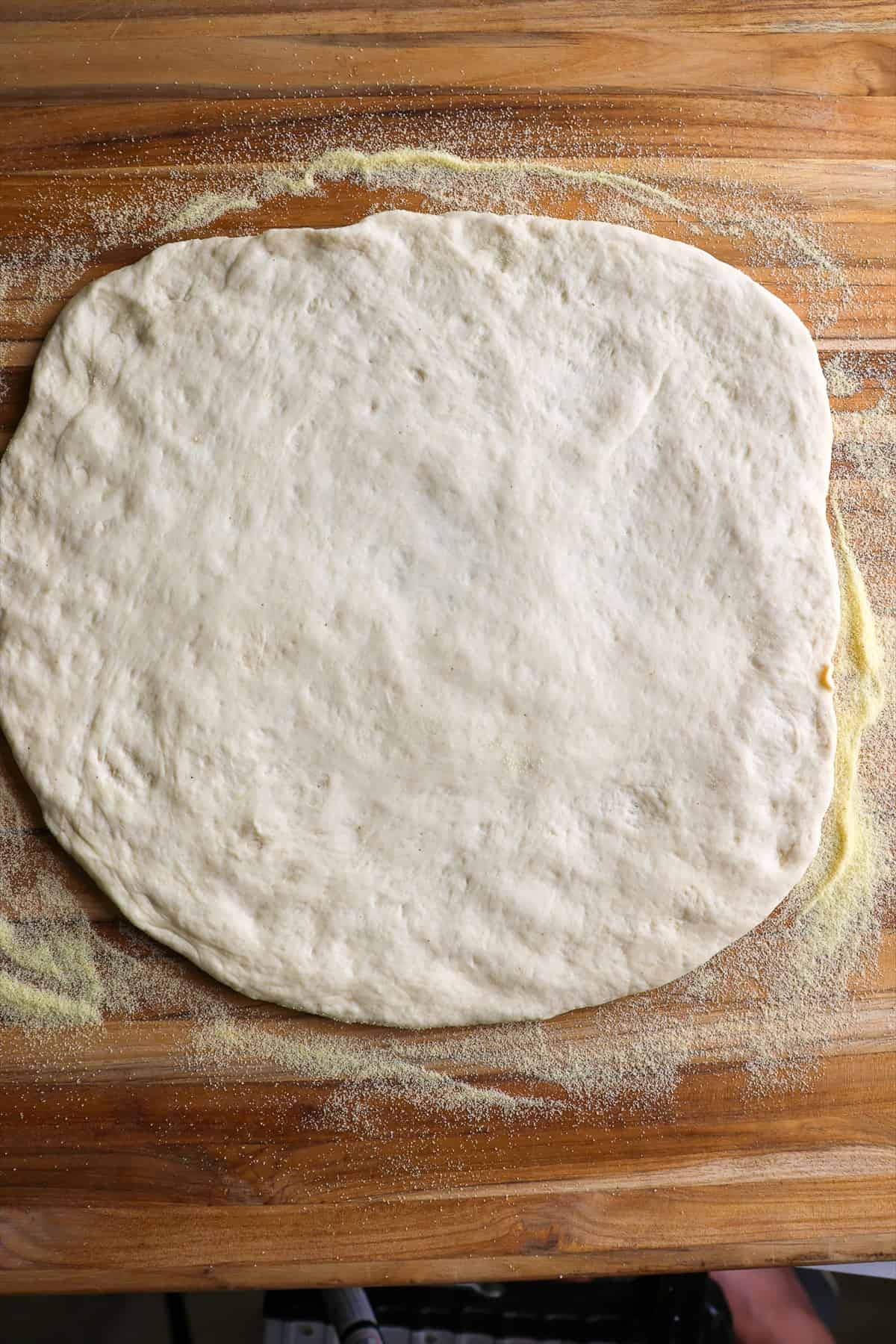 Pizza dough stretched into a round on a semolina dusted cutting board.