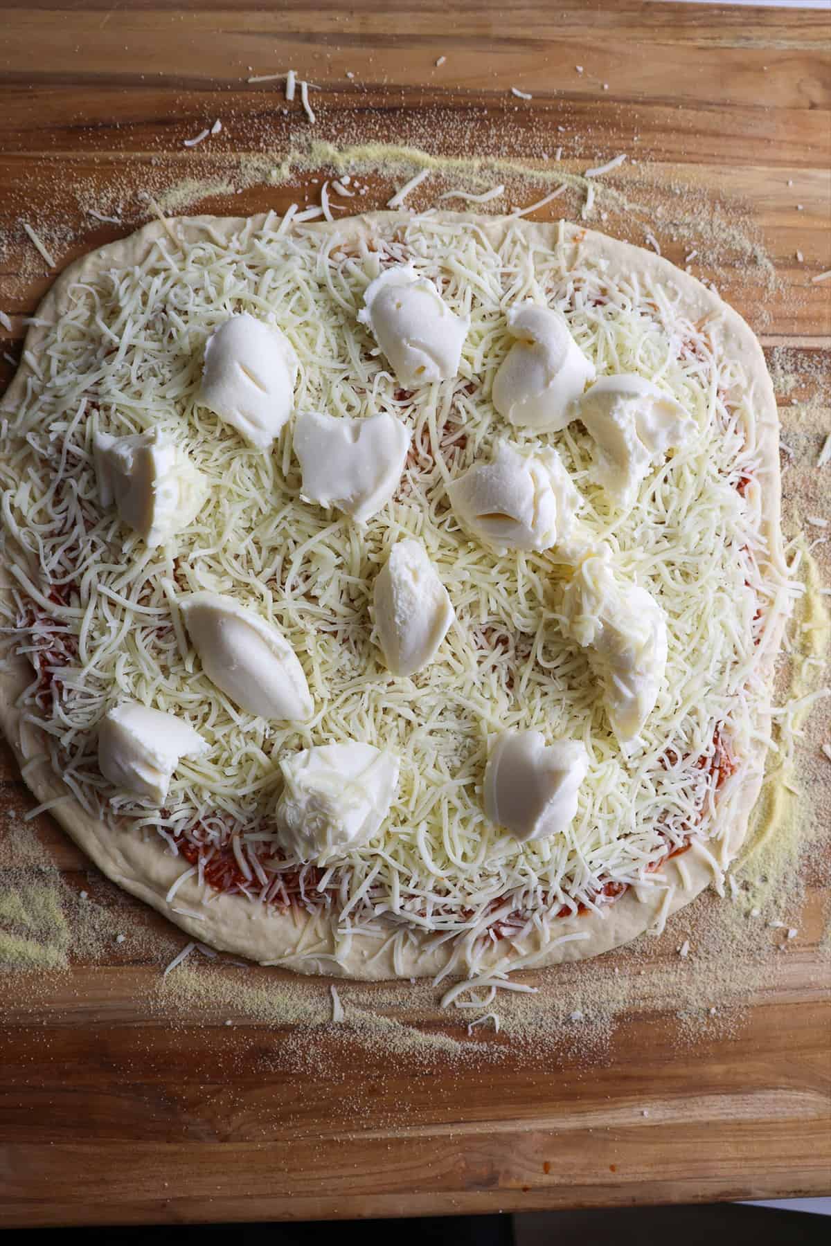 Unbaked pizza topped with sauce, shredded mozzarella, Parmesan, and spoonfuls of ricotta on a pizza peel.