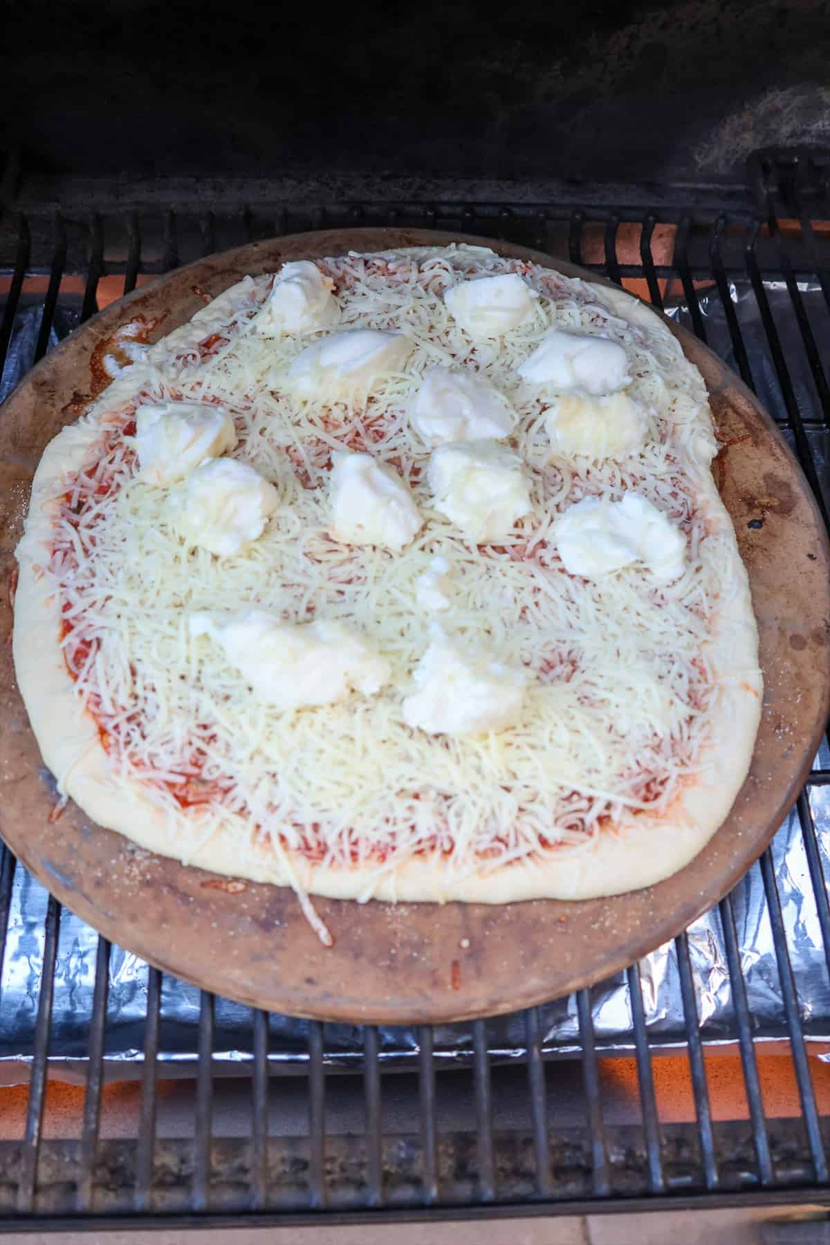 Three cheese pizza cooking on a preheated pizza stone inside the smoker.