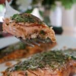 A fork lifting a flaky bite from this cedar plank Smoked Salmon Recipe topped with fresh dill and parsley.