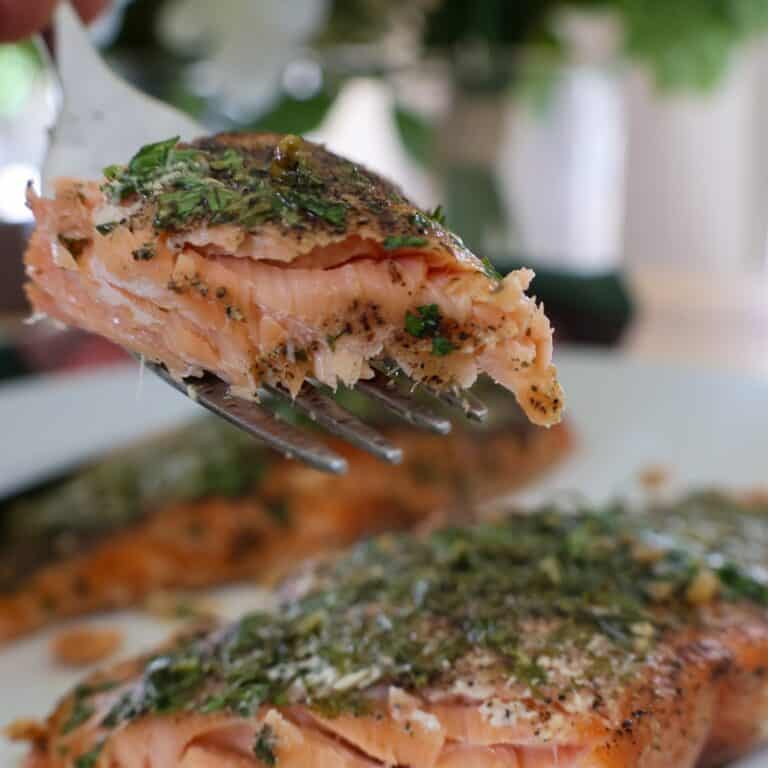 A fork lifting a flaky bite from this cedar plank Smoked Salmon Recipe topped with fresh dill and parsley.