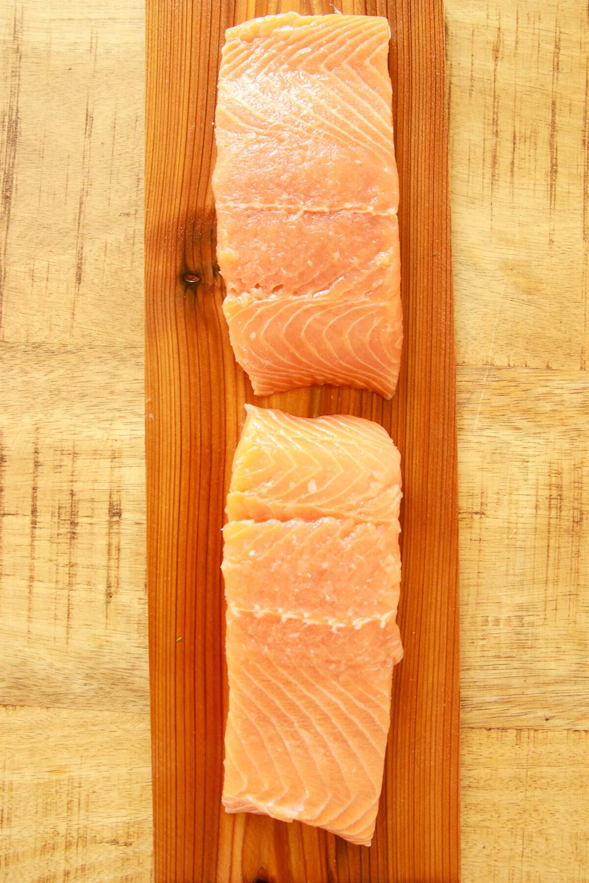 Raw salmon fillets rubbed with olive oil laying skin side down on a soaked cedar plank.