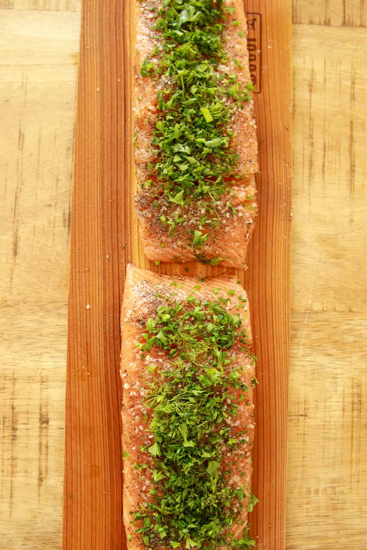 Salmon fillets on a cedar plank seasoned with salt, pepper, chopped fresh dill, and parsley.